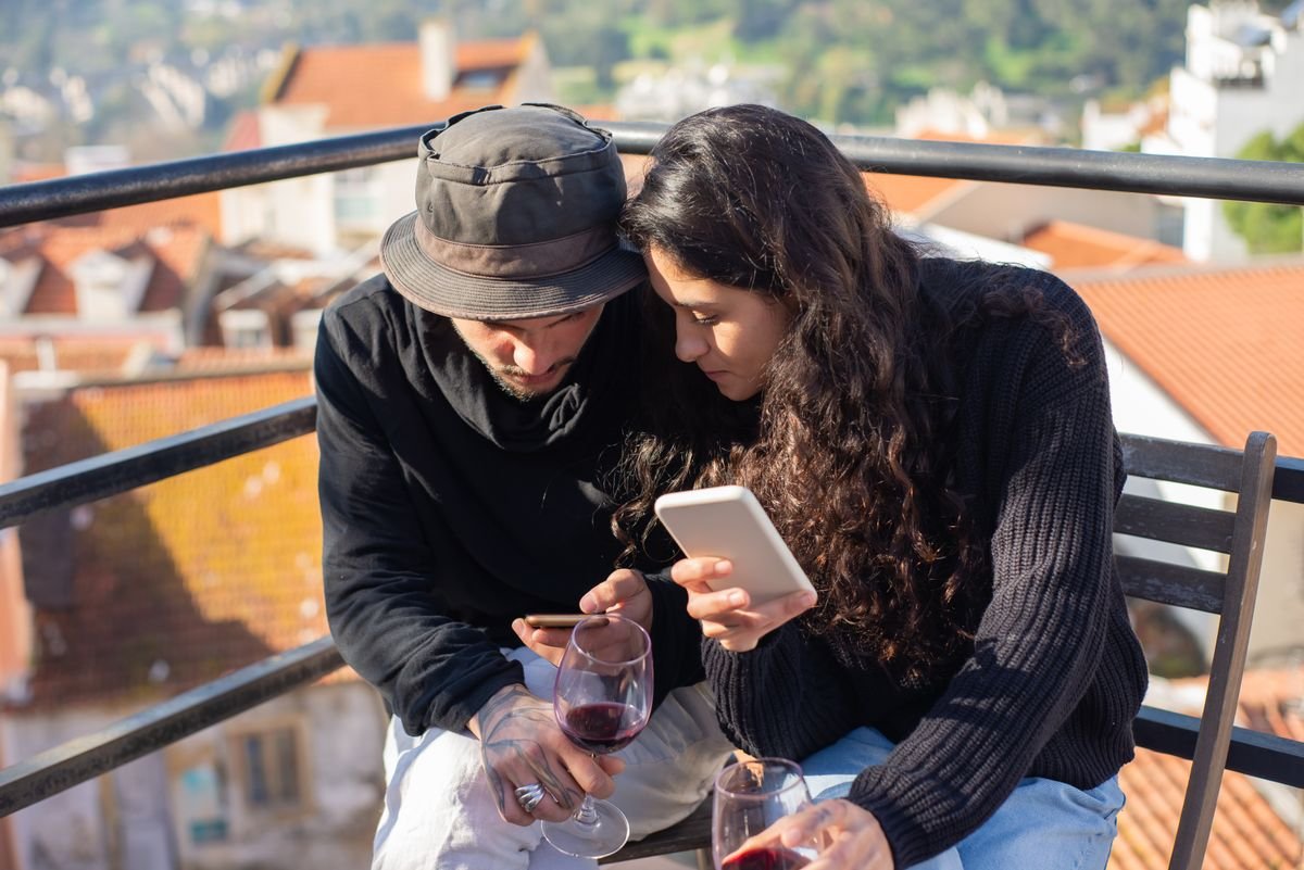 Couple looking at their phones together on a sunny balcony
