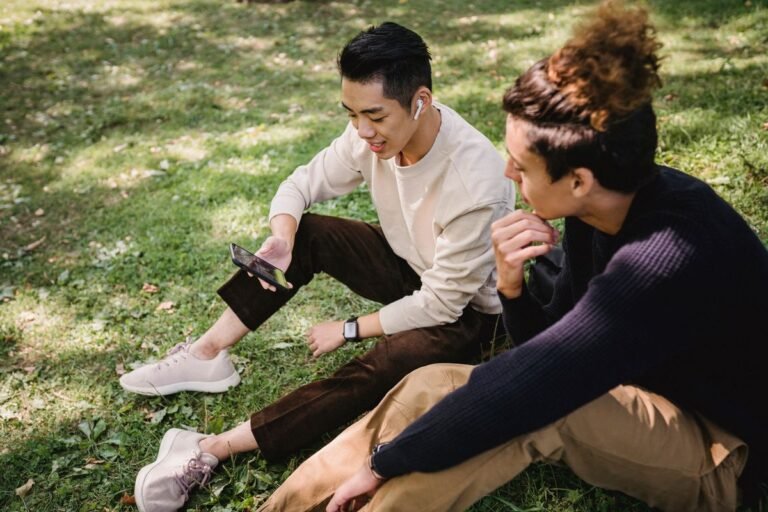 Two friends watching a video on a phone while sitting on the grass