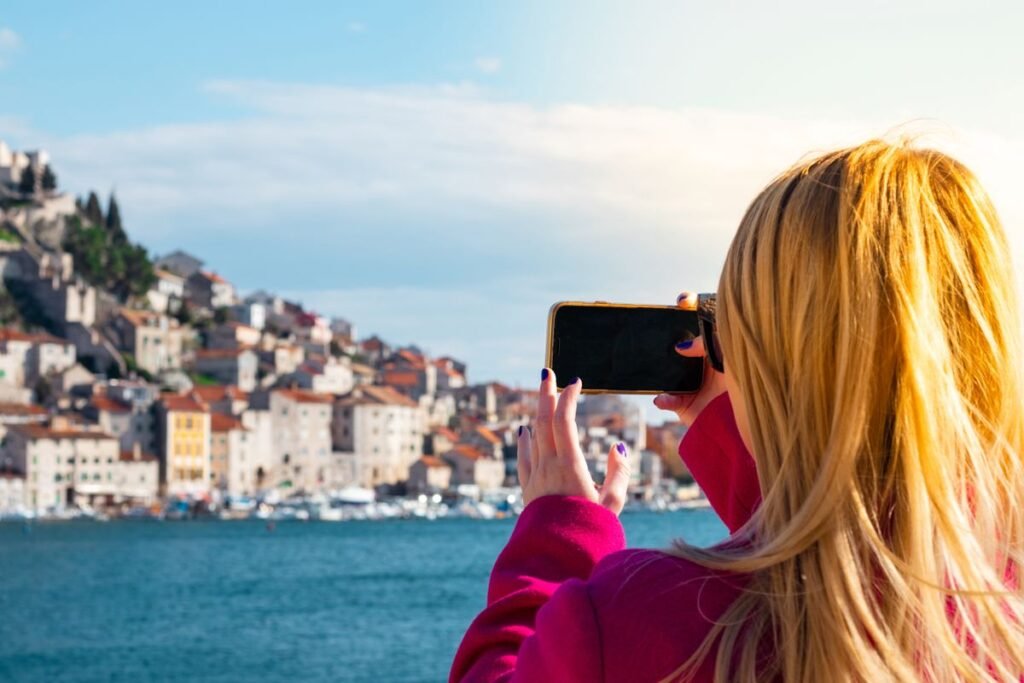 Traveller taking a photo of a coastal European town with her phone