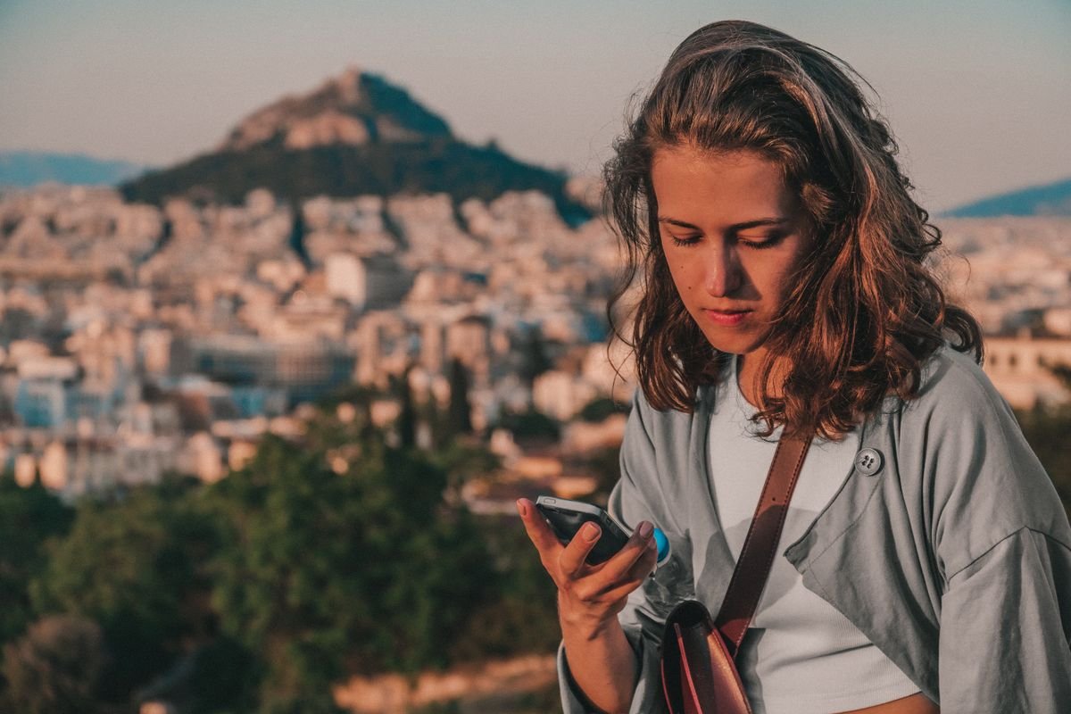 Woman checking her phone with a hillside city in the background